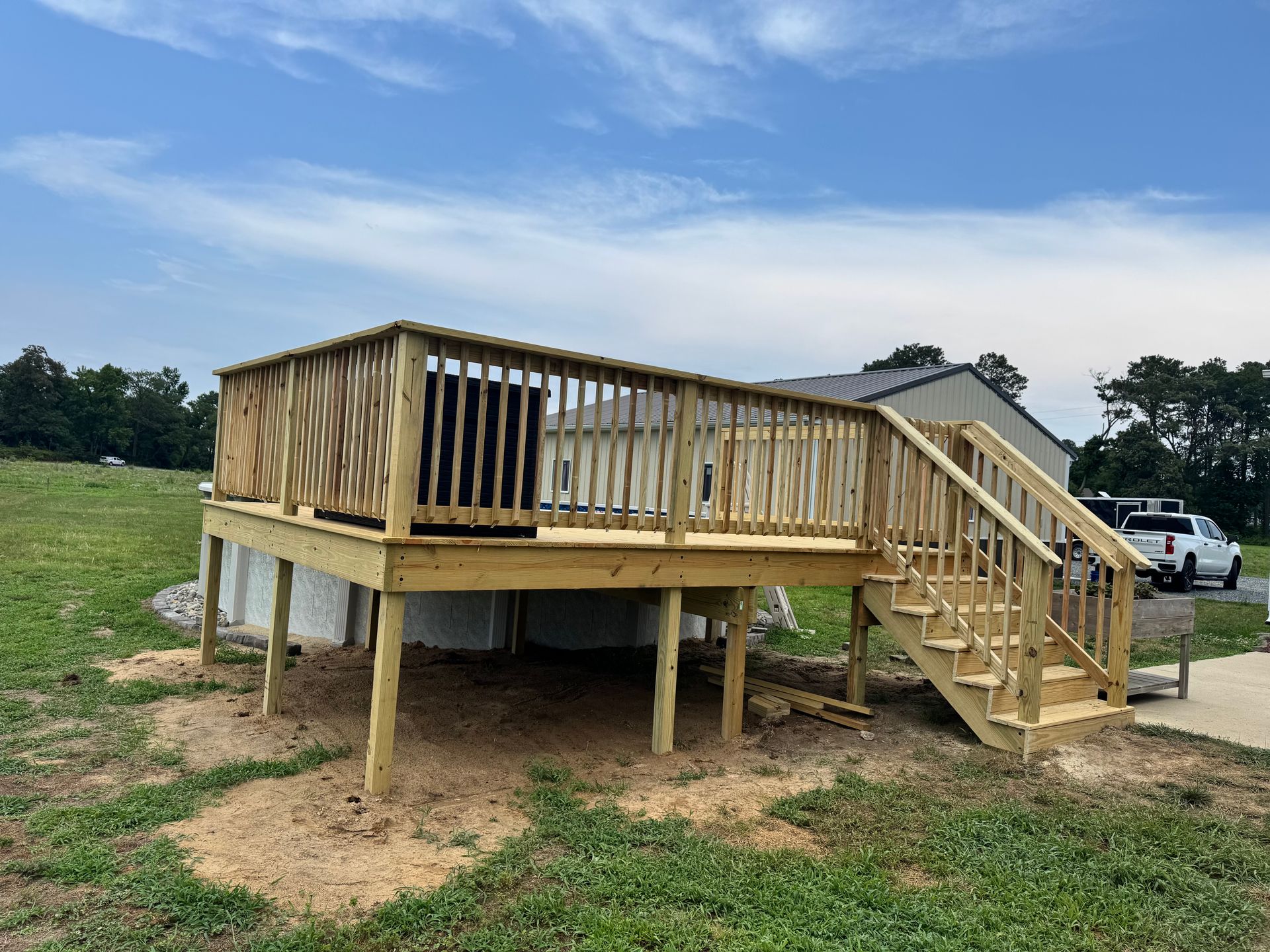 Wooden raised deck under construction with stairs, set on a grassy lot under a blue sky.