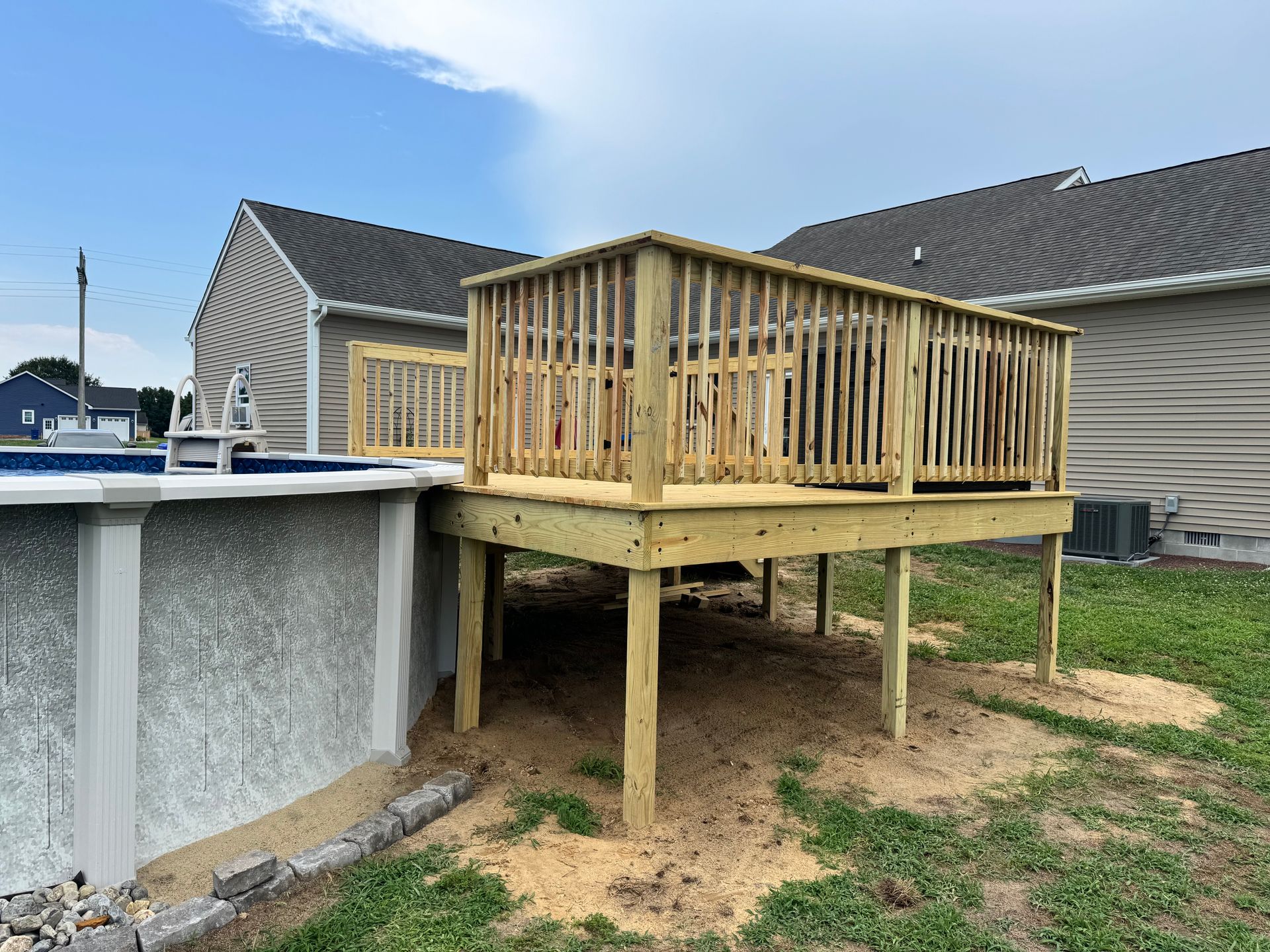 Wooden raised deck under construction beside a backyard aboveground pool, with support posts and framing exposed