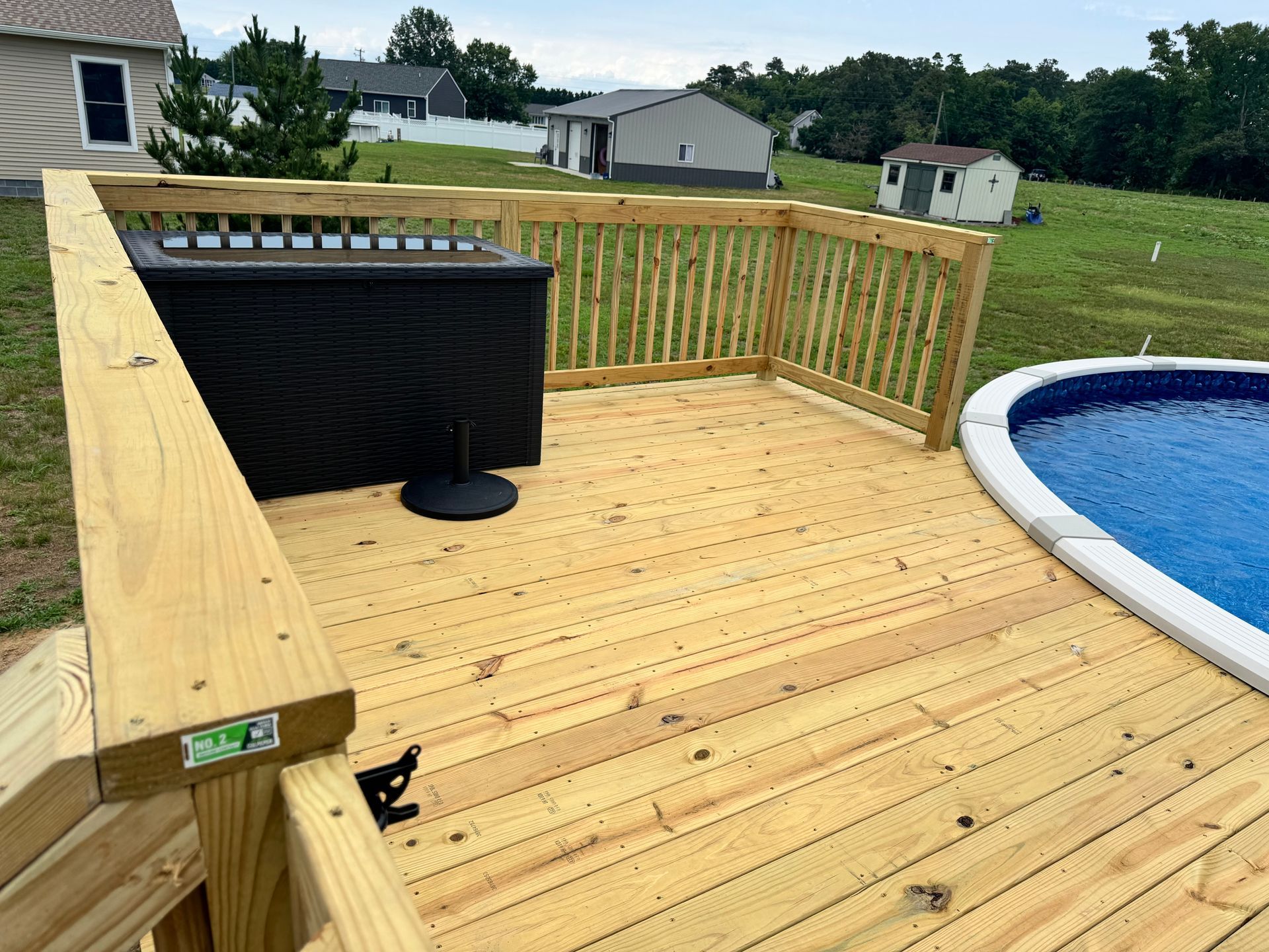 Wooden deck beside an above-ground pool, with railings and a black bar table and stools.