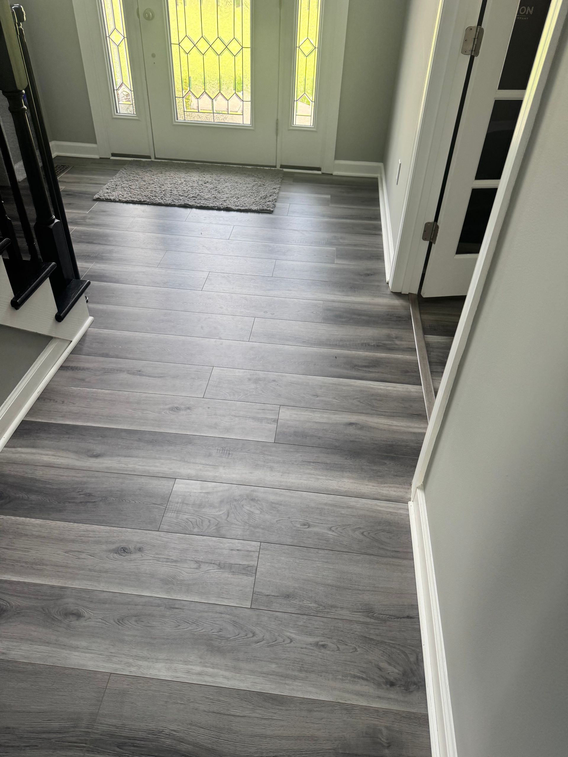 Hallway with gray wood flooring leading to a front door with frosted glass panels.