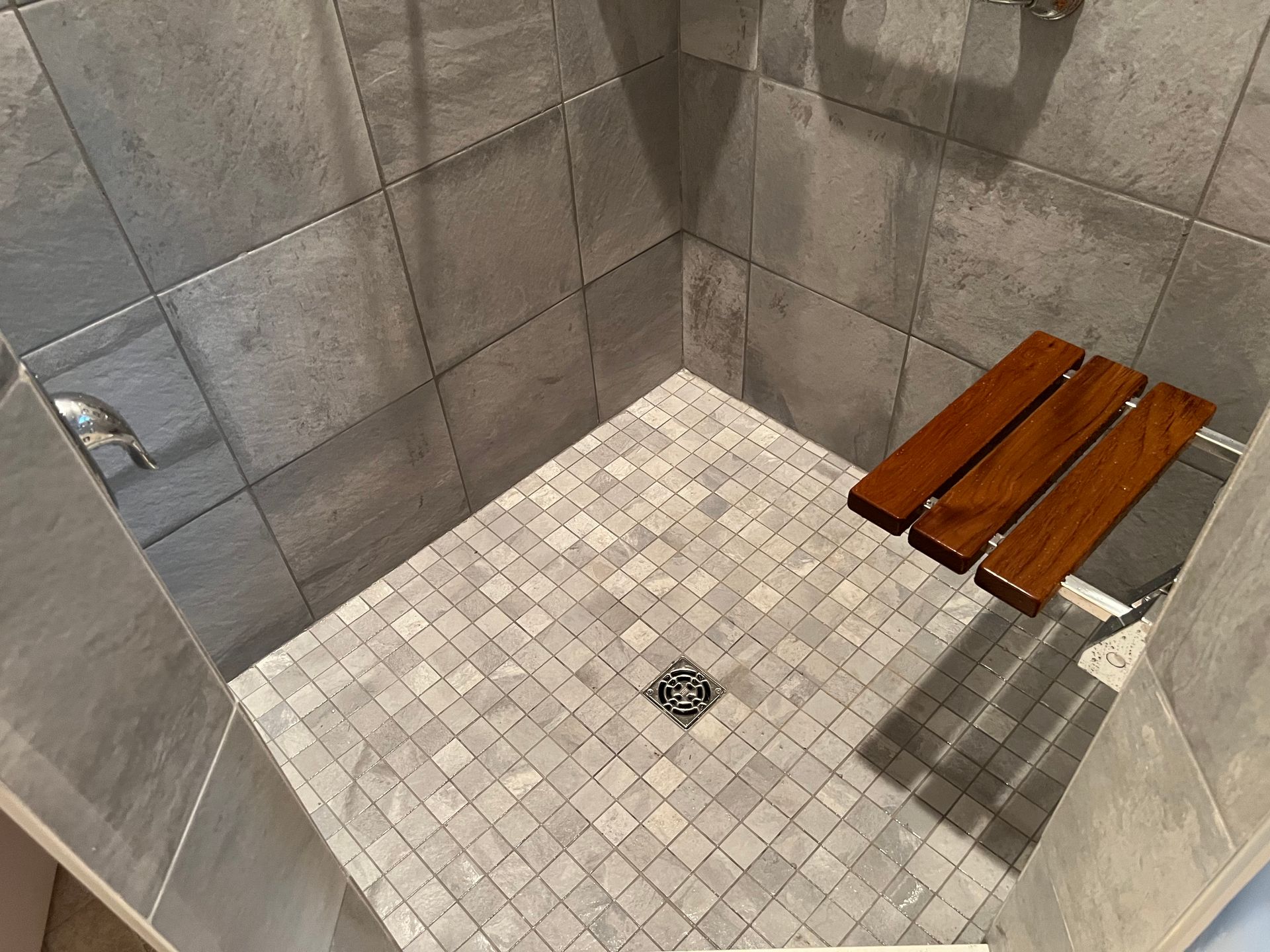 Walk-in tiled shower with wooden bench and central drain