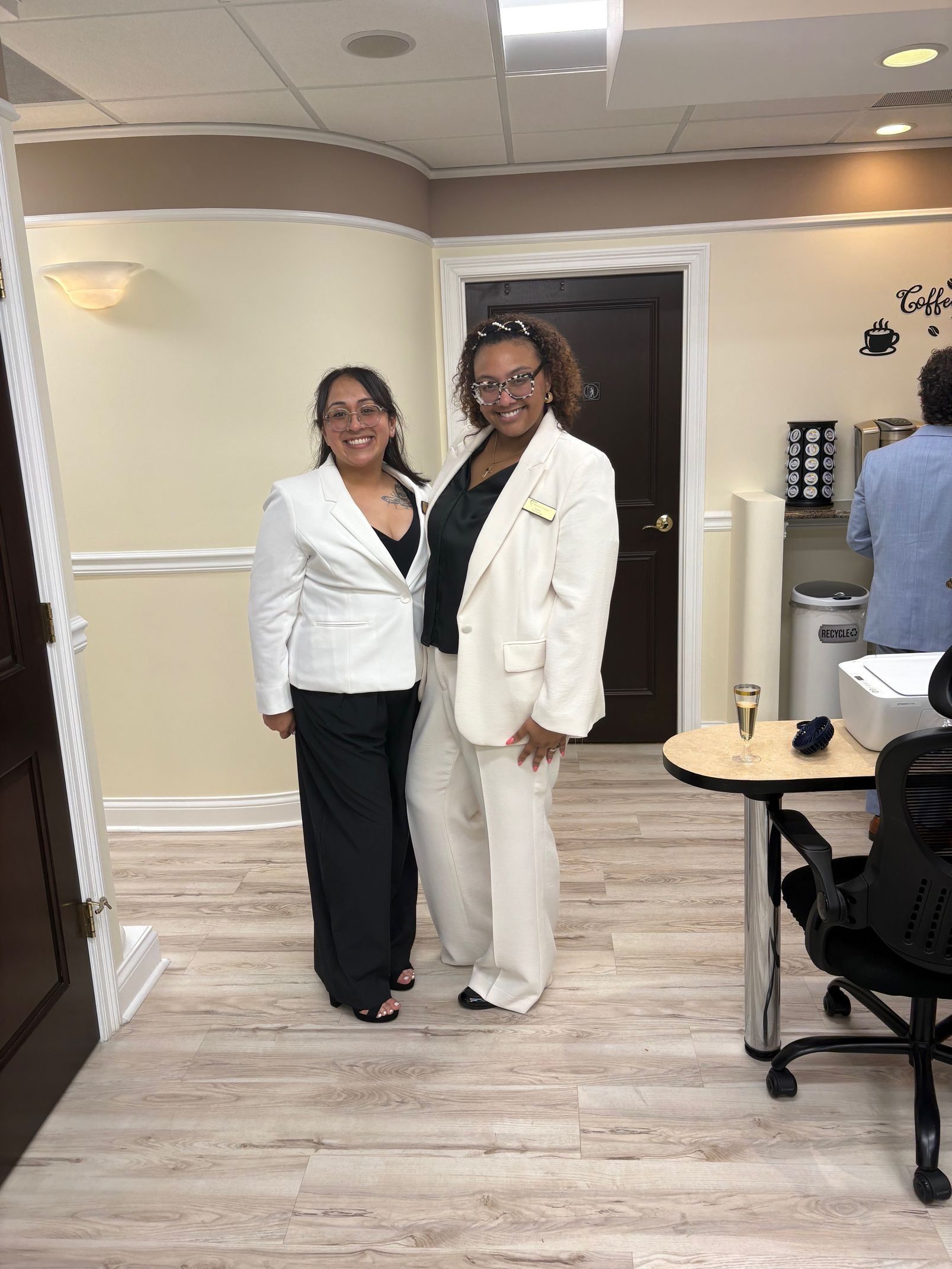 Two women in business attire pose inside an office.