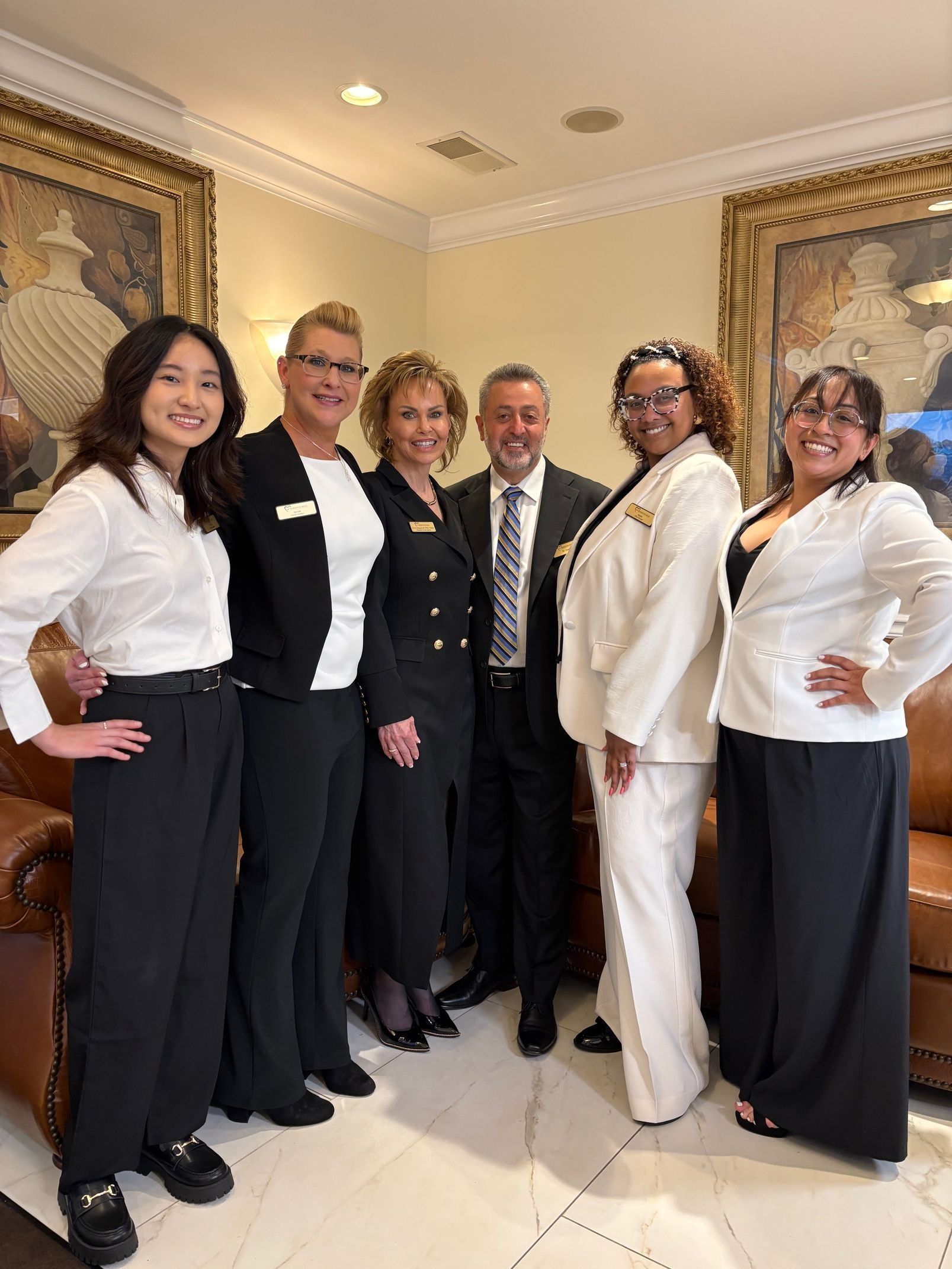 Group of six people posing in formal attire in a room with ornate decor.