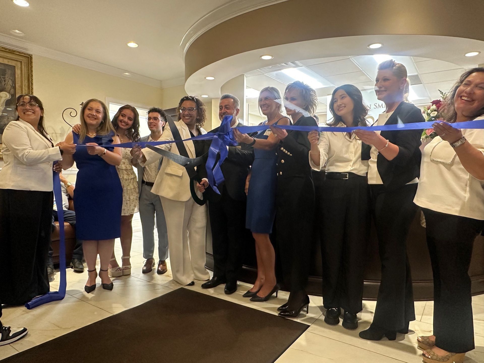 People cutting a blue ribbon at a business opening. They are smiling. Interior setting.