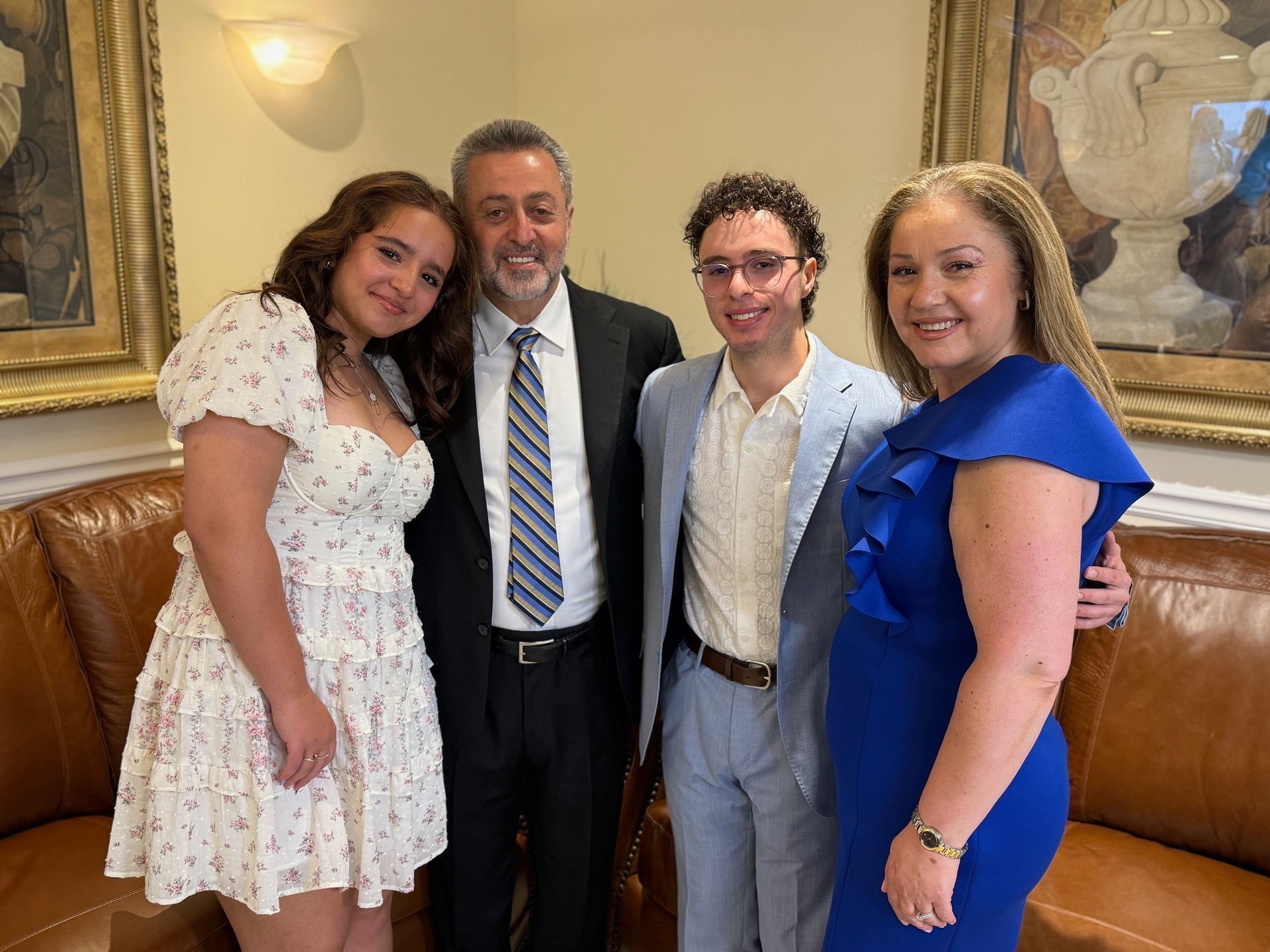 Family of four smiling, posing indoors. Woman in blue dress, man in suit, teens.