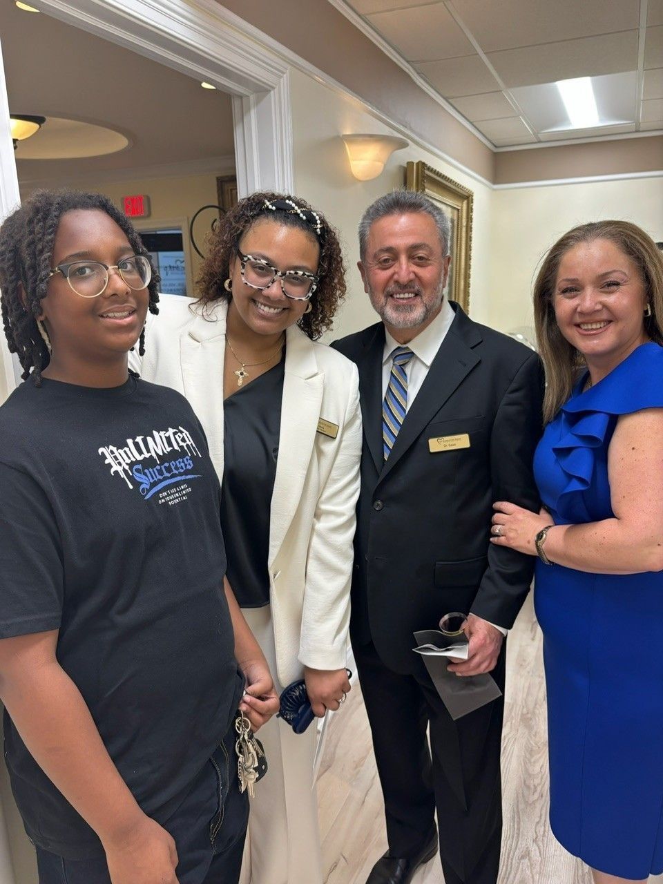 Four people pose for a photo in a warmly lit room. Two women and a man are in business attire, one woman wears a graphic tee.