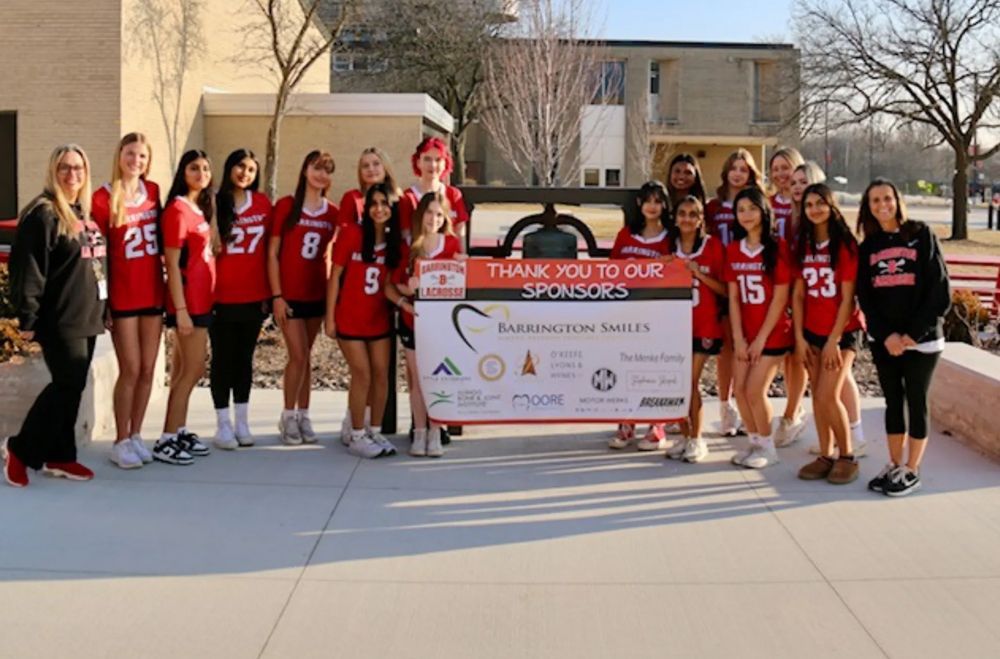 Group of girls in red jerseys holding a "Thank you" sign, outdoors in front of a building.