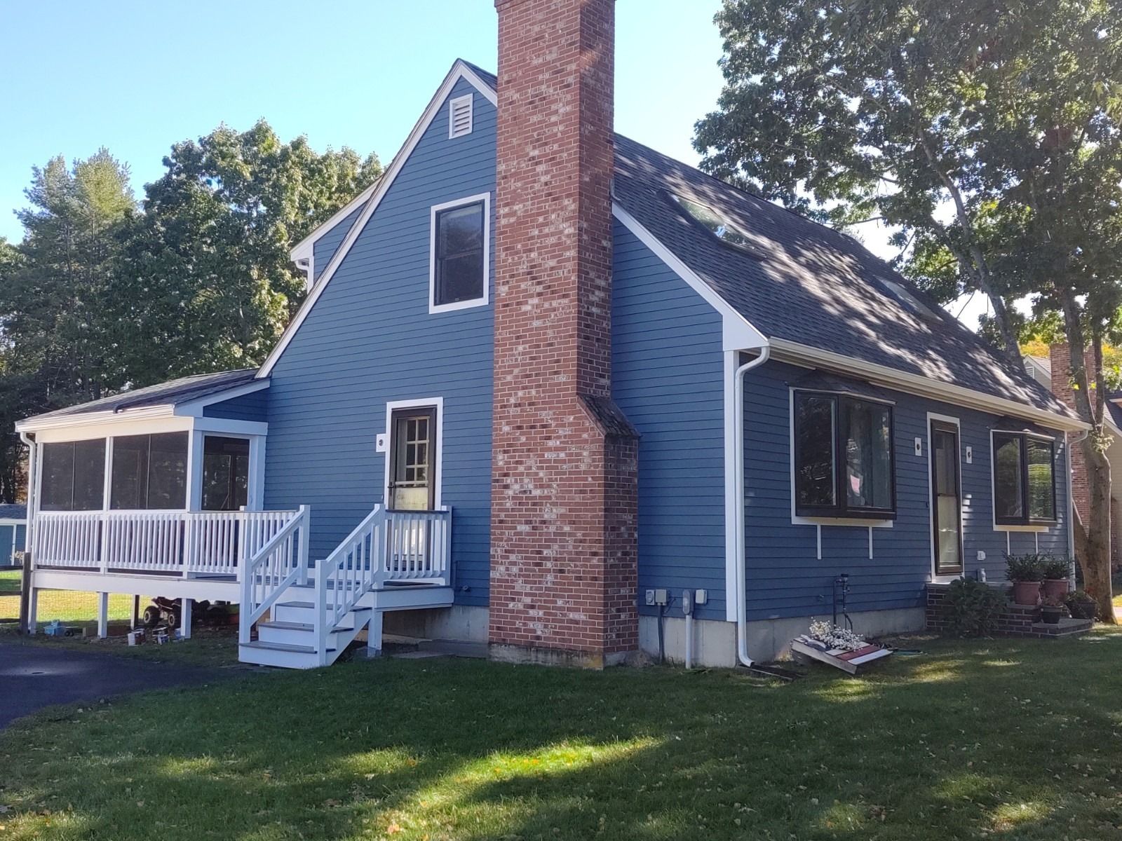Blue house with a brick chimney, porch, and a yard.
