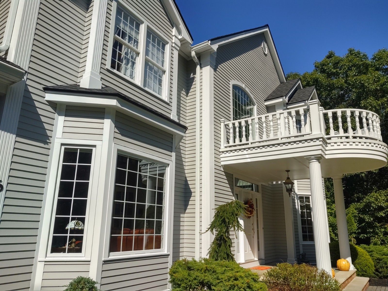 Gray house with white trim, bay window, balcony, and blue sky.