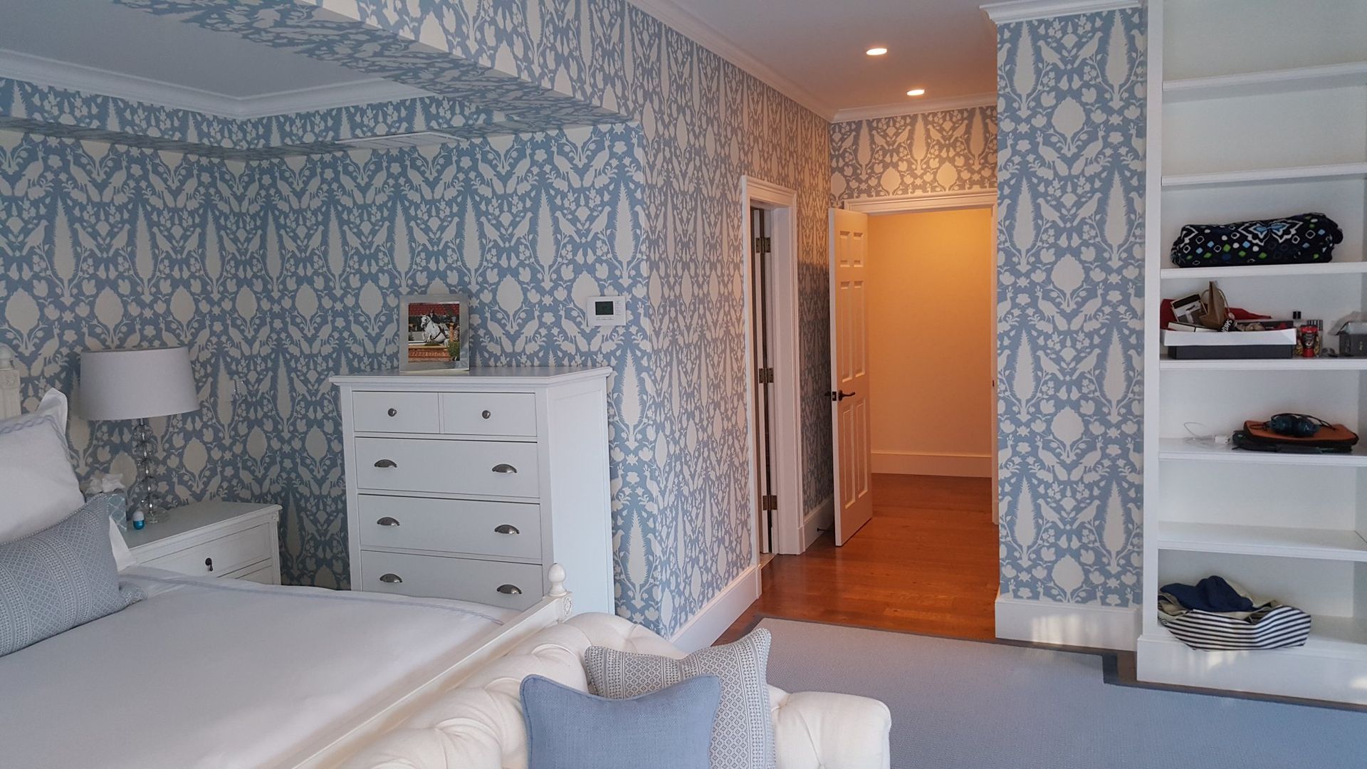 Bedroom with blue and white patterned wallpaper, a white dresser, and built-in shelving.