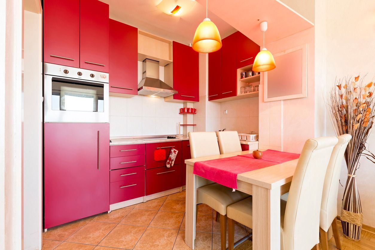 Red and white kitchen with dining area, featuring cabinets, appliances, table, chairs, and hanging lights.