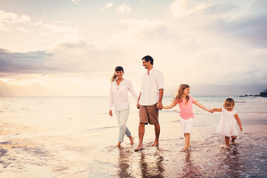 Family holding hands, walking along a beach at sunset.