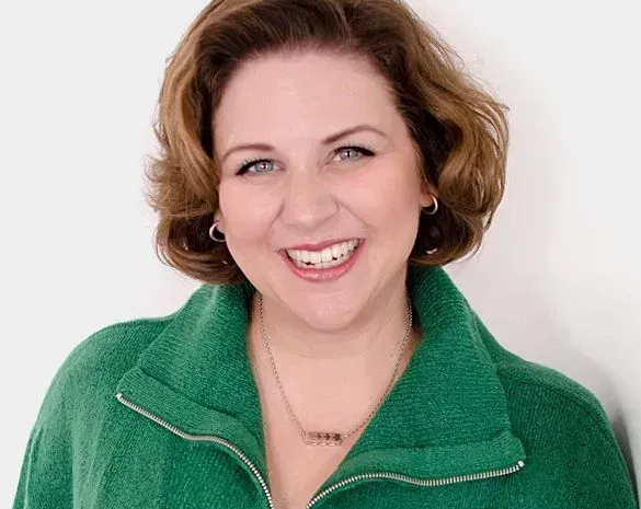 A woman in a green jacket smiles at the camera against a white background.