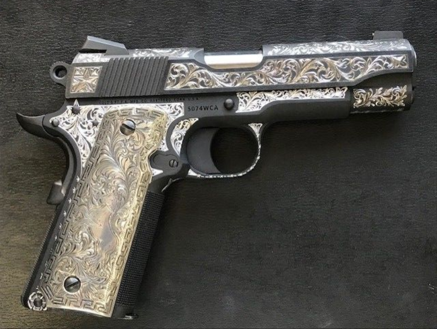 Engraved silver and black handgun on a dark surface.