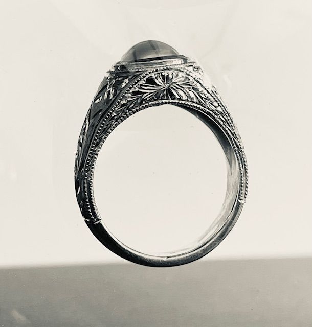 Silver ring with engraved floral and leaf design, set with a rounded gem.