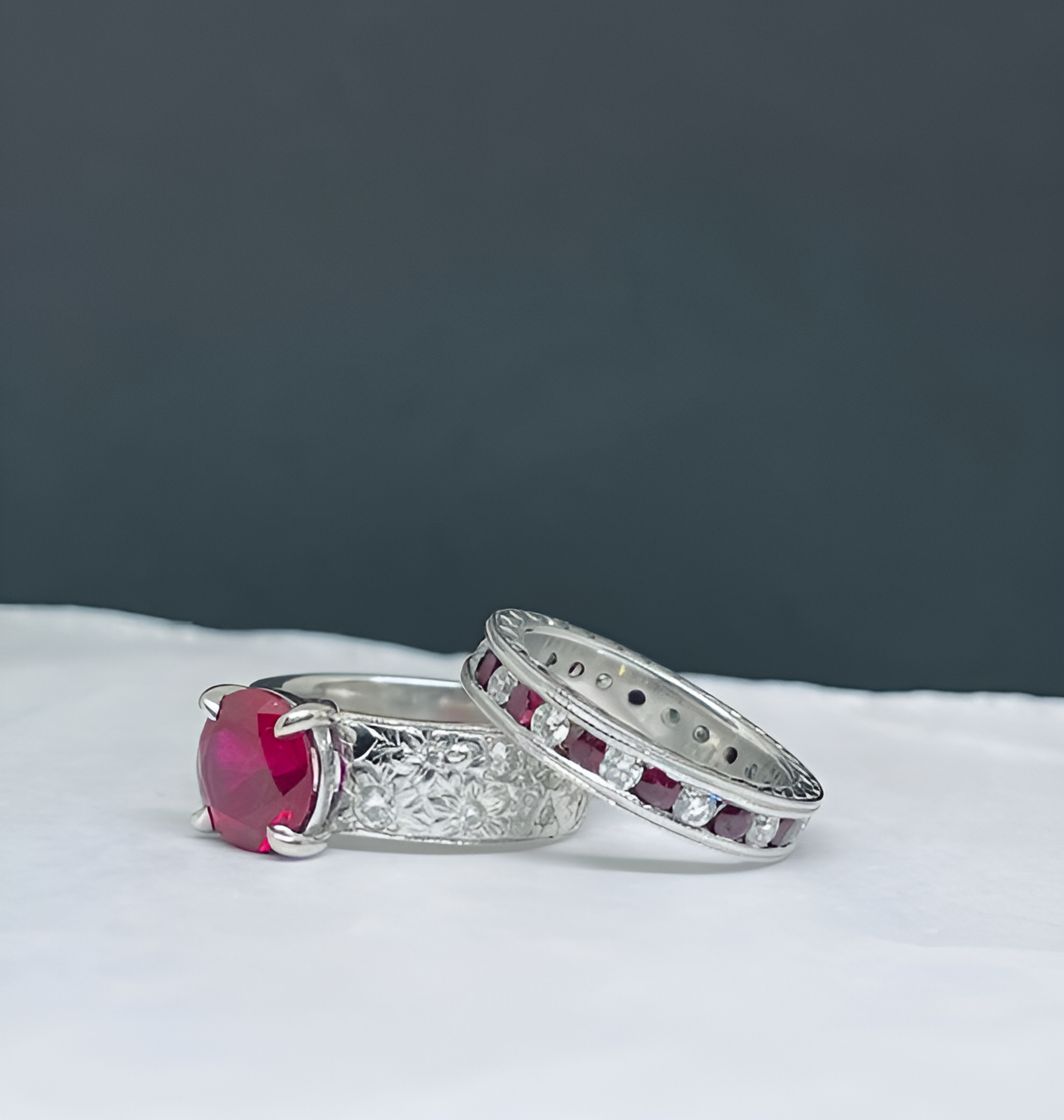 Two ruby rings on a white surface, one with a large central stone, the other an eternity band.