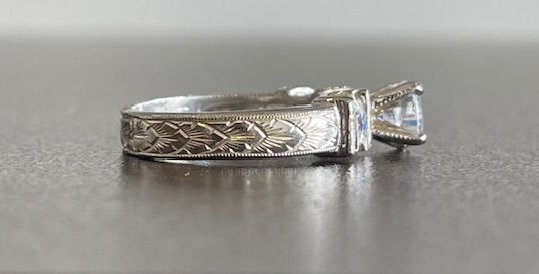 A silver engagement ring with a square-cut diamond and engraved band.