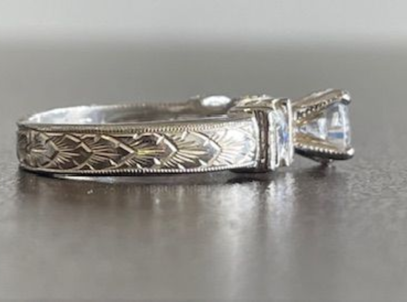 Close-up of a silver engagement ring with a large square gemstone and engraved band.