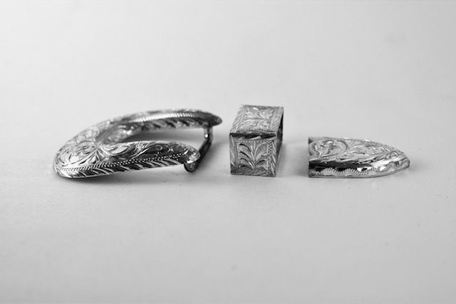 Three ornate silver metal buckle pieces on a white surface.