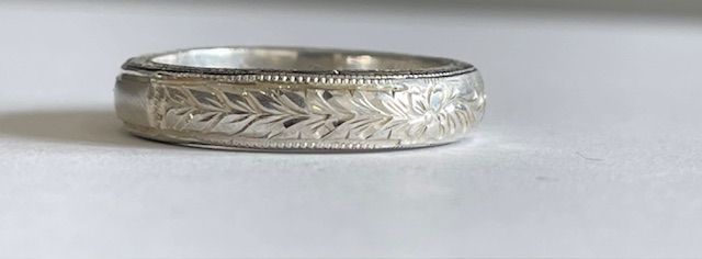 Silver ring with etched leaf design, resting on a white surface.