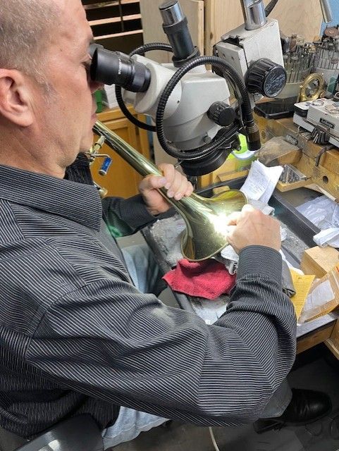 Man working with a brass instrument under a microscope in a workshop.
