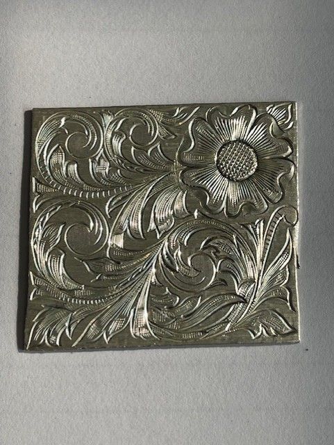 Silver rectangular metal plate with intricate floral engraving.