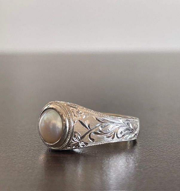 Silver ring with a pearl set in the center. Floral pattern engraved on the band.
