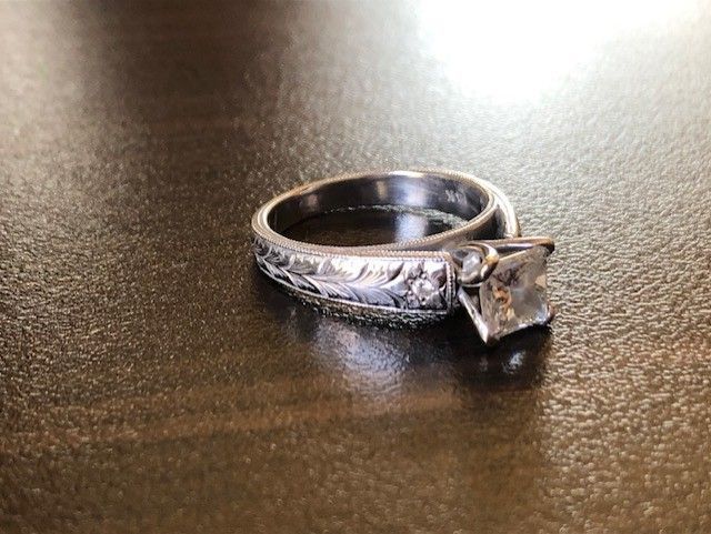 Diamond engagement ring with ornate detailing on a reflective surface.