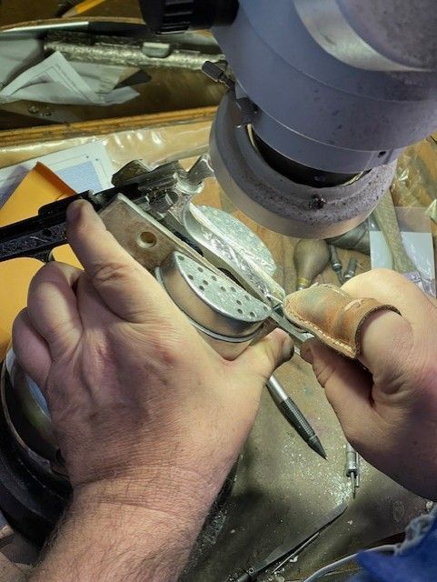 Hands using a tool to grind metal component under grinding machine.
