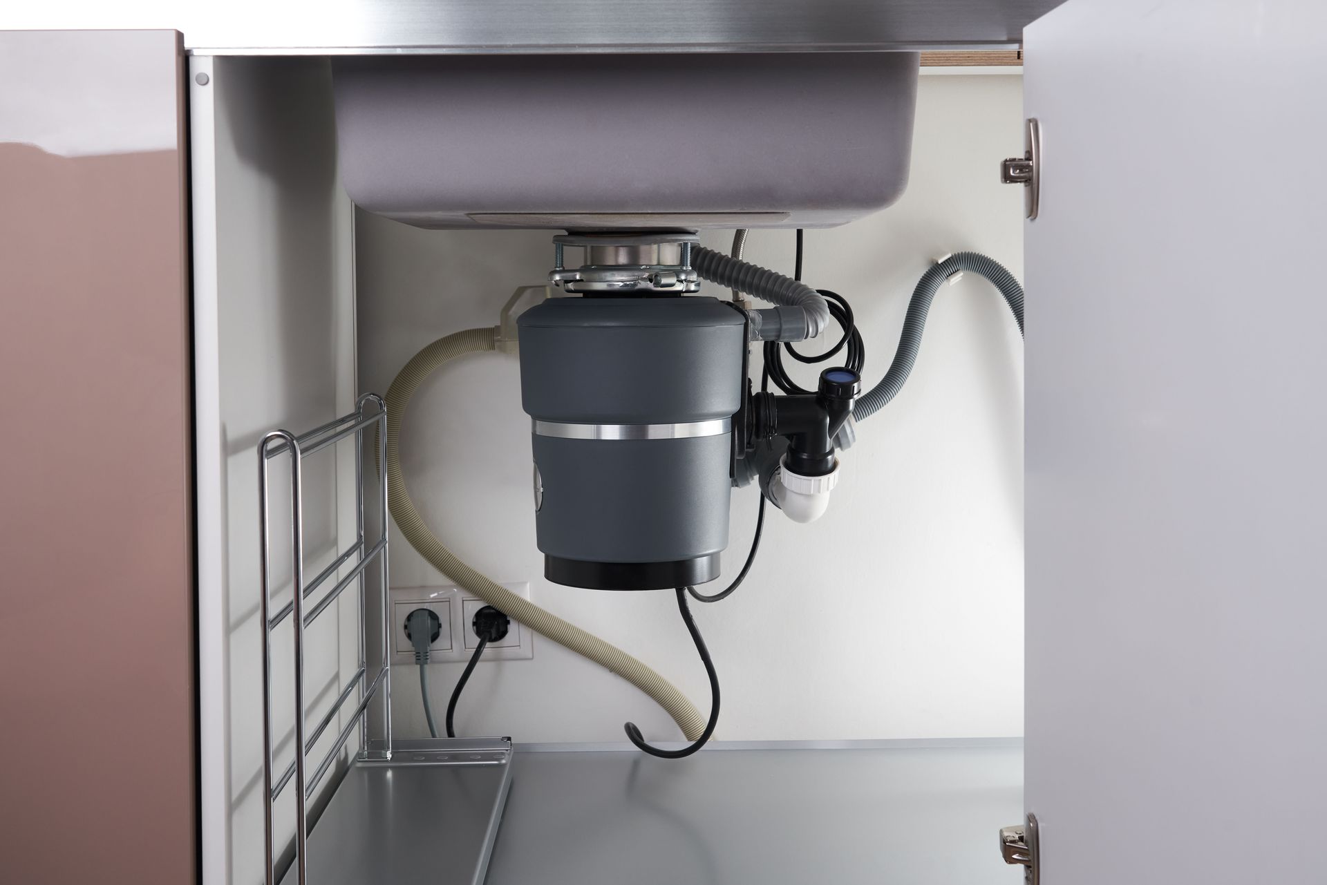 Garbage disposal unit under a kitchen sink. Gray disposal, white cabinet, plumbing visible.