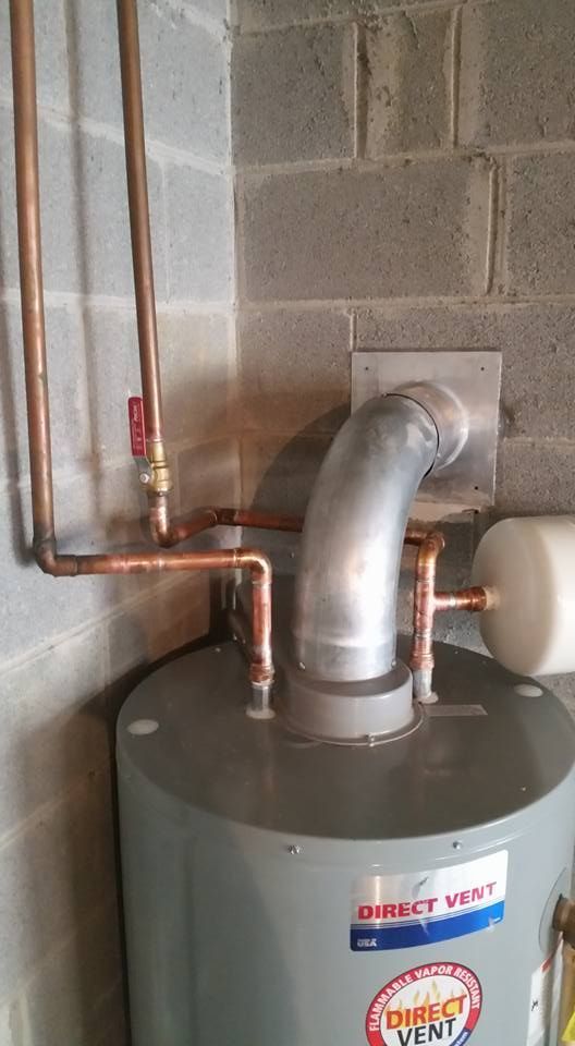 A water heater is sitting in a room next to a brick wall.