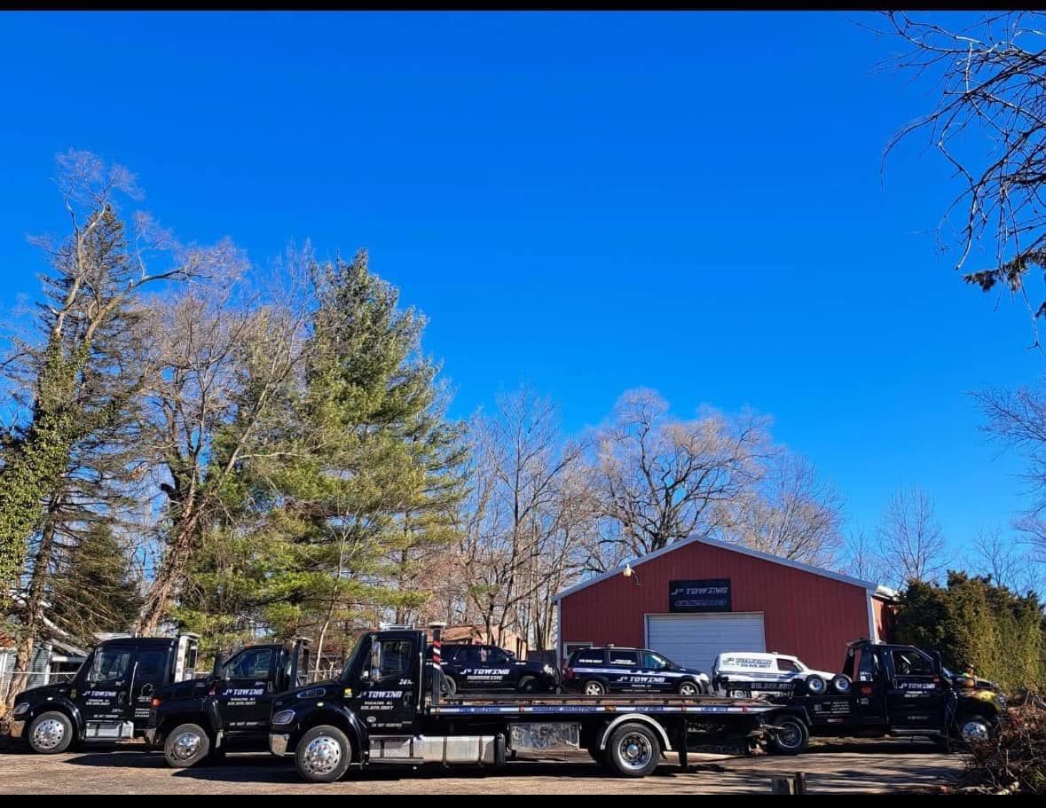 Three tow trucks are parked in front of a red barn.