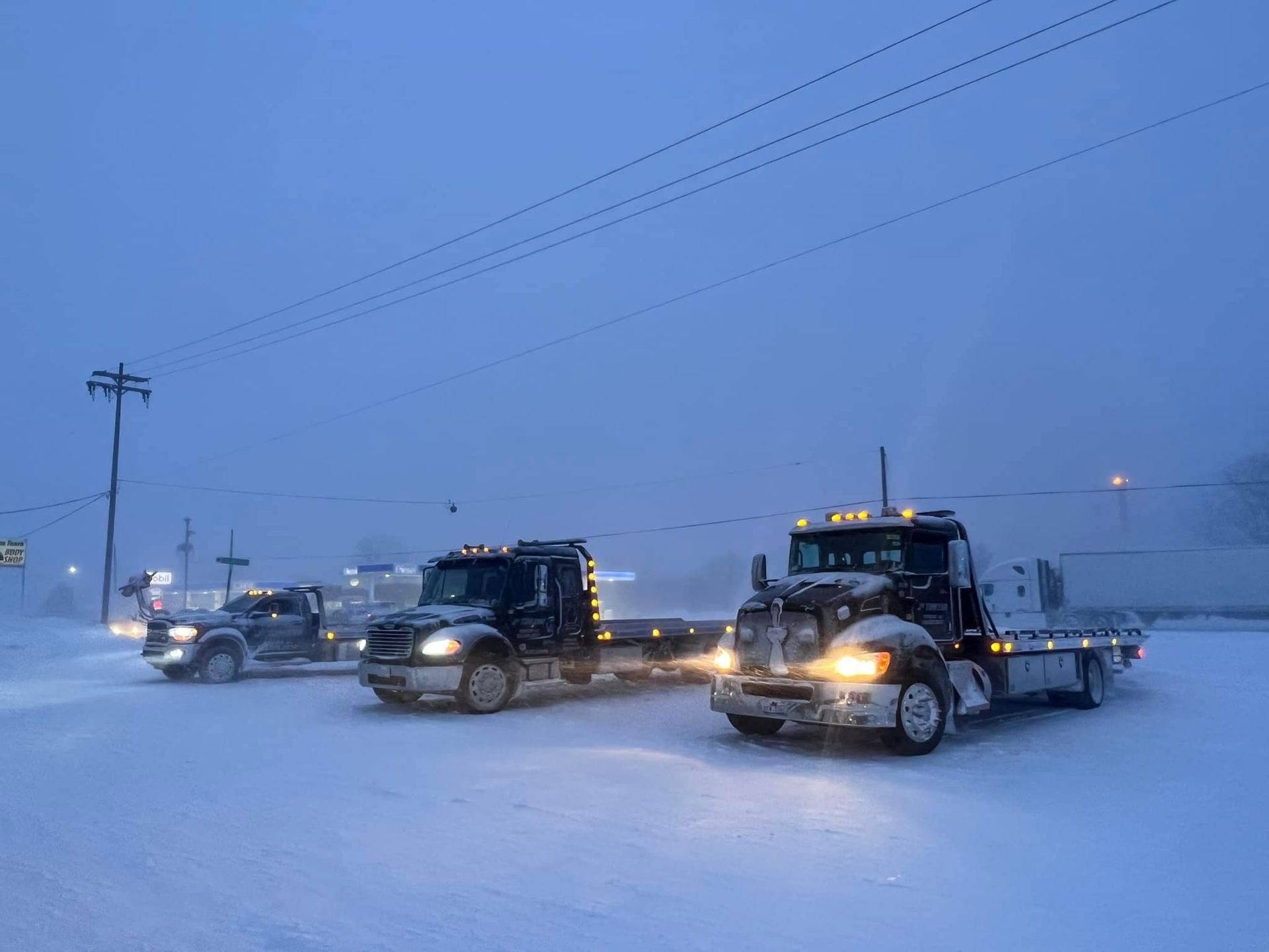 Two tow trucks are driving down a snowy road.