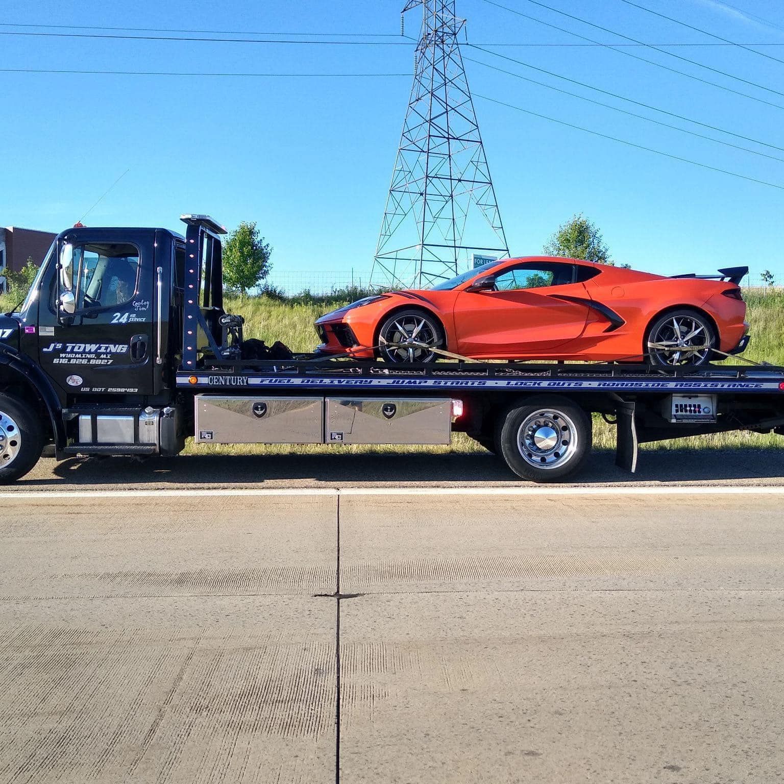 A tow truck is carrying a red sports car on the back of it.