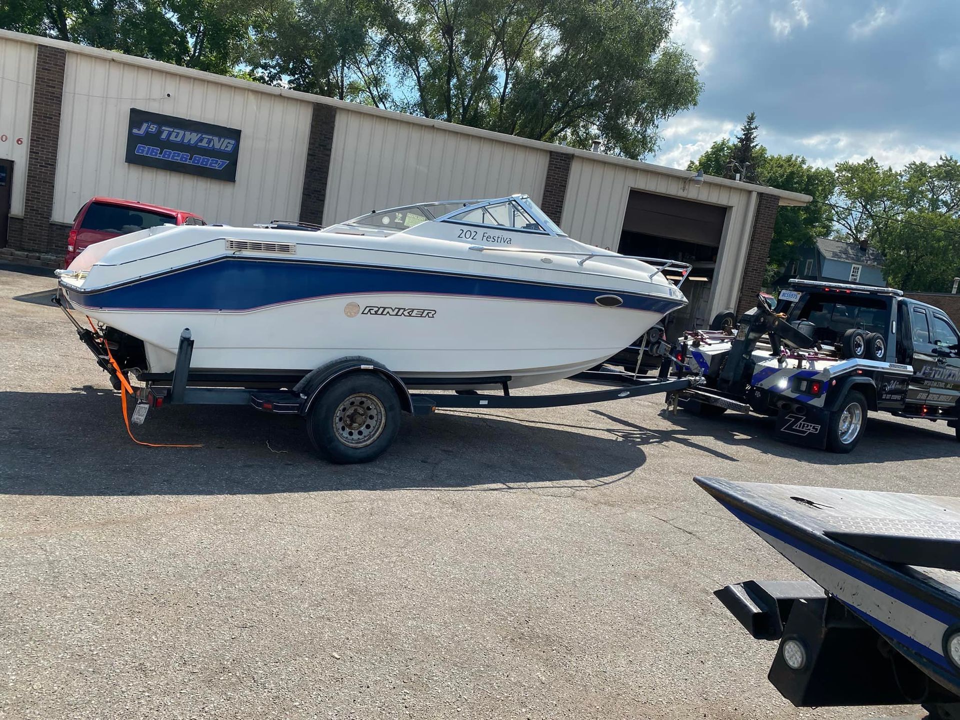 A white and blue boat on a trailer is parked in front of a building.