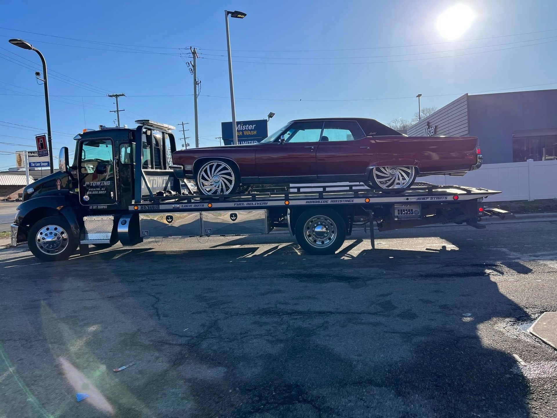 A tow truck is carrying a red car on the back of it.