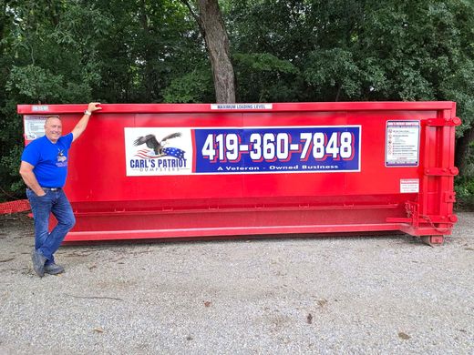 Man standing beside a red dumpster with a large 419-360-7848 sign outdoors