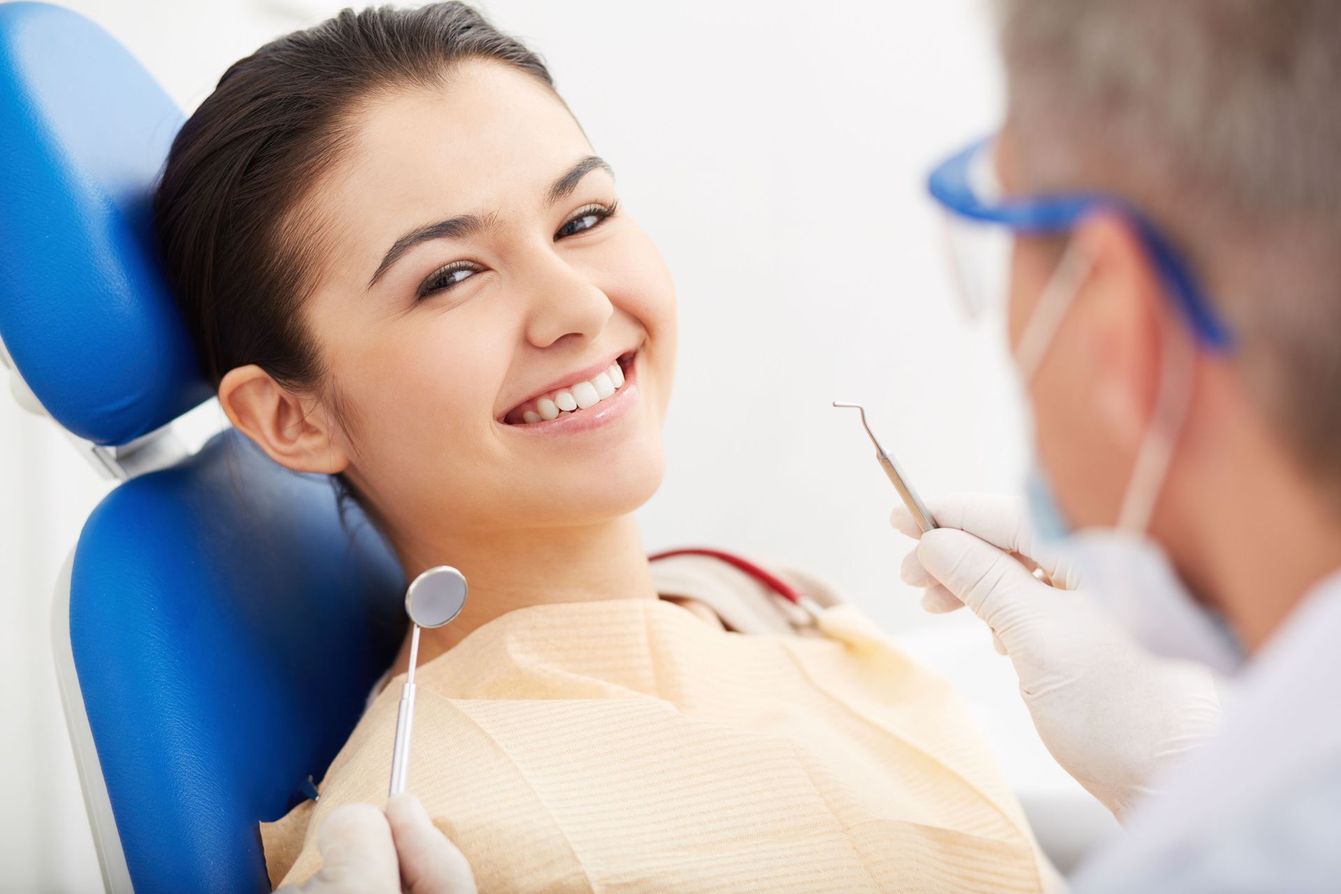 Smiling dental patient in chair as dentist examines teeth with tools
