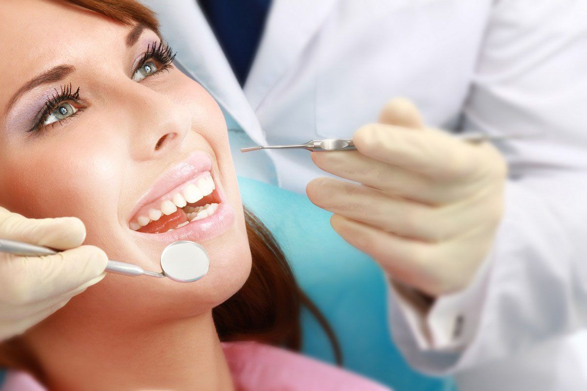 Dentist examining a smiling patient’s teeth with mirror and probe in a dental chair