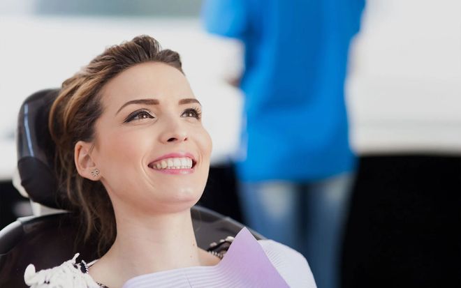 Smiling woman reclining in a dental chair while holding a pink folder