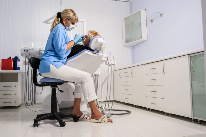 Dentist examining a patient in a clean, bright clinic, with cabinets and equipment nearby.