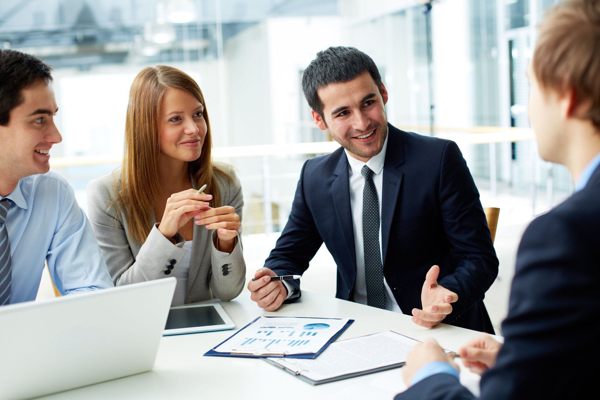 Business meeting with four people discussing documents around a table in a bright office
