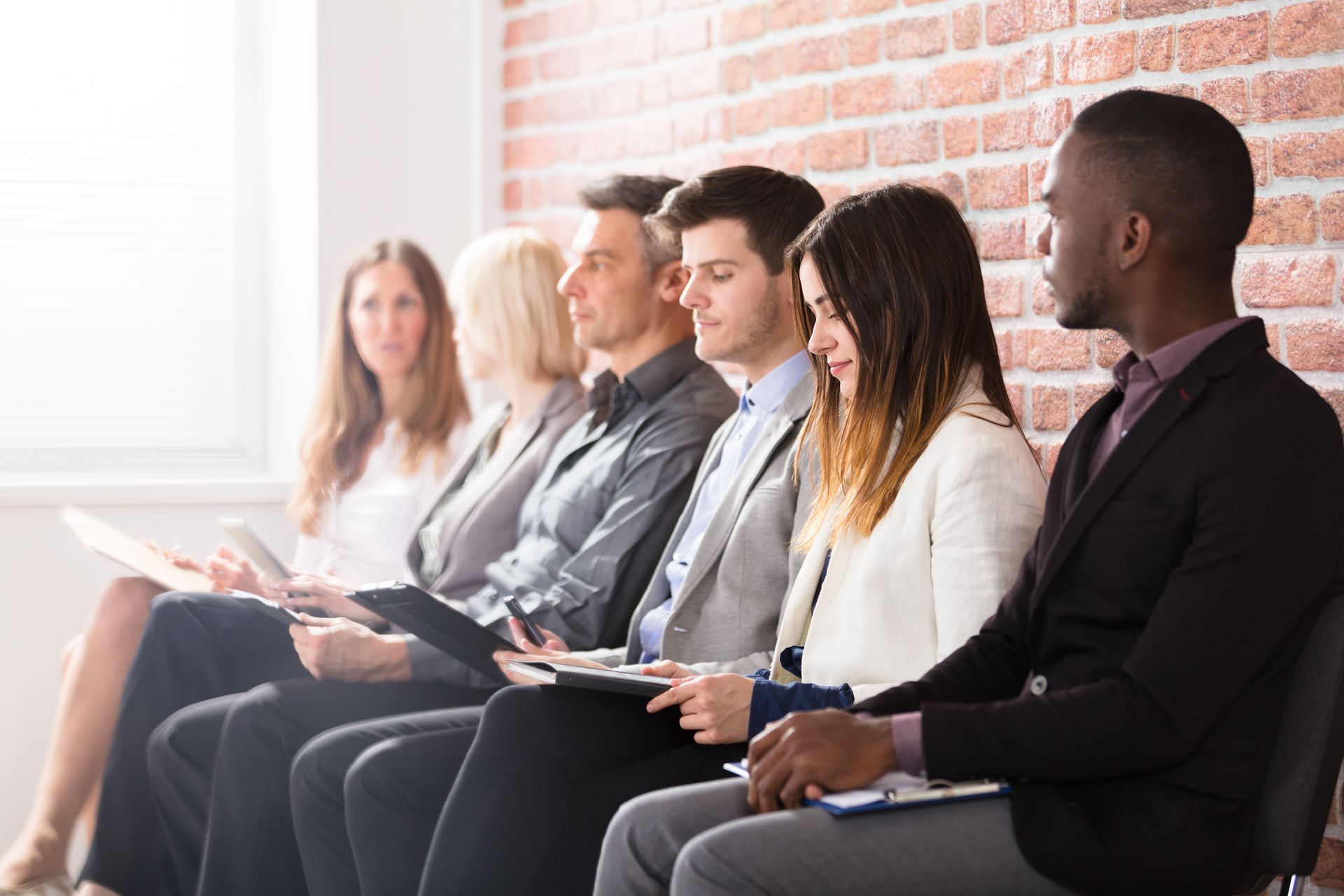 People seated in a row during a business meeting, taking notes in a bright office.