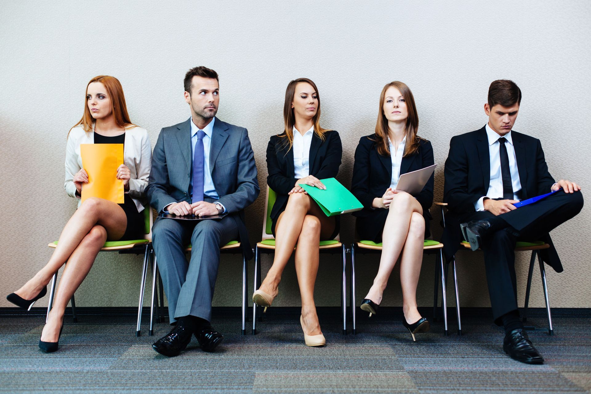 Five office workers seated in a row, holding folders and waiting in a lobby.