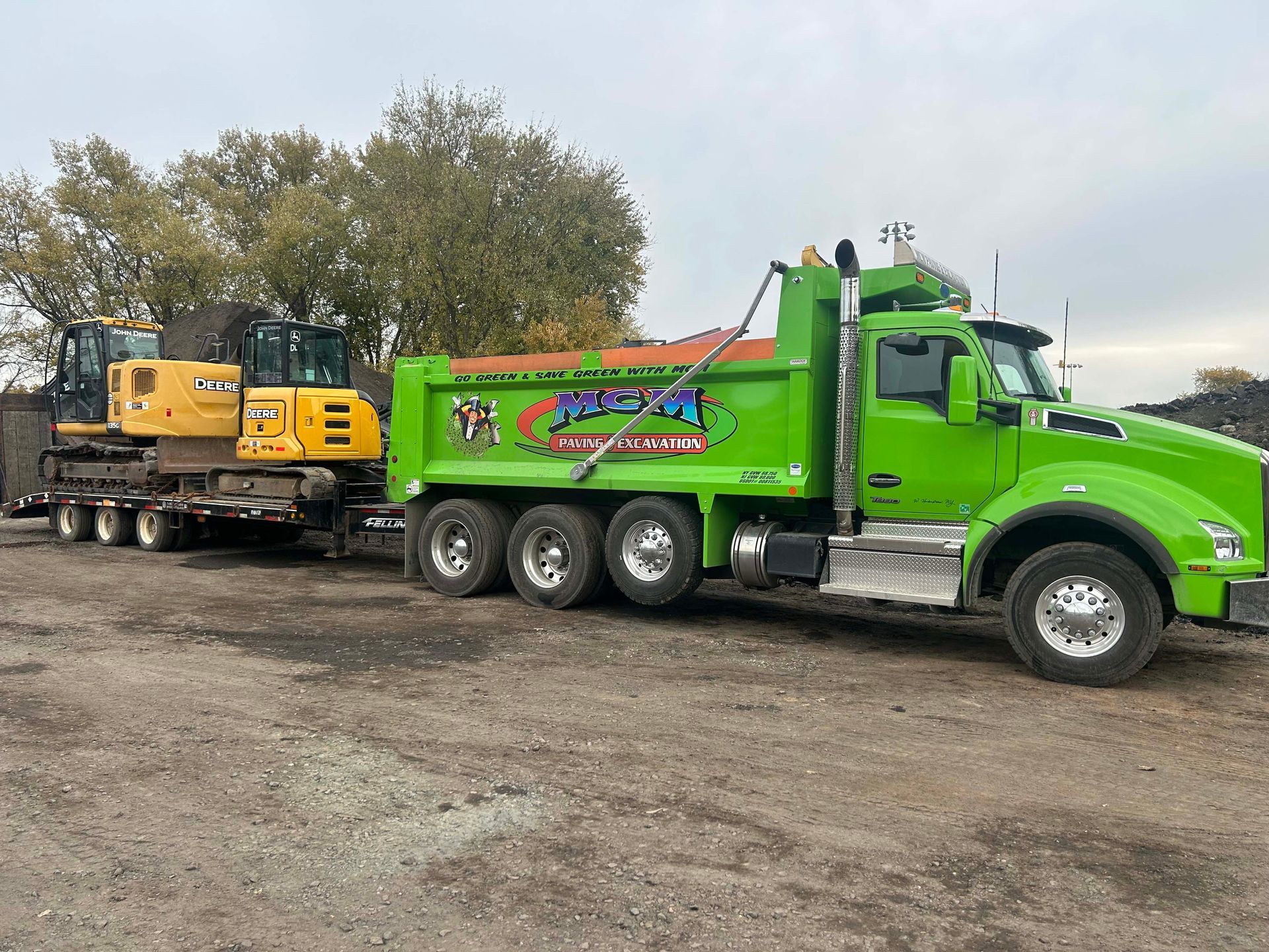 A green dump truck is towing a yellow excavator on a trailer.