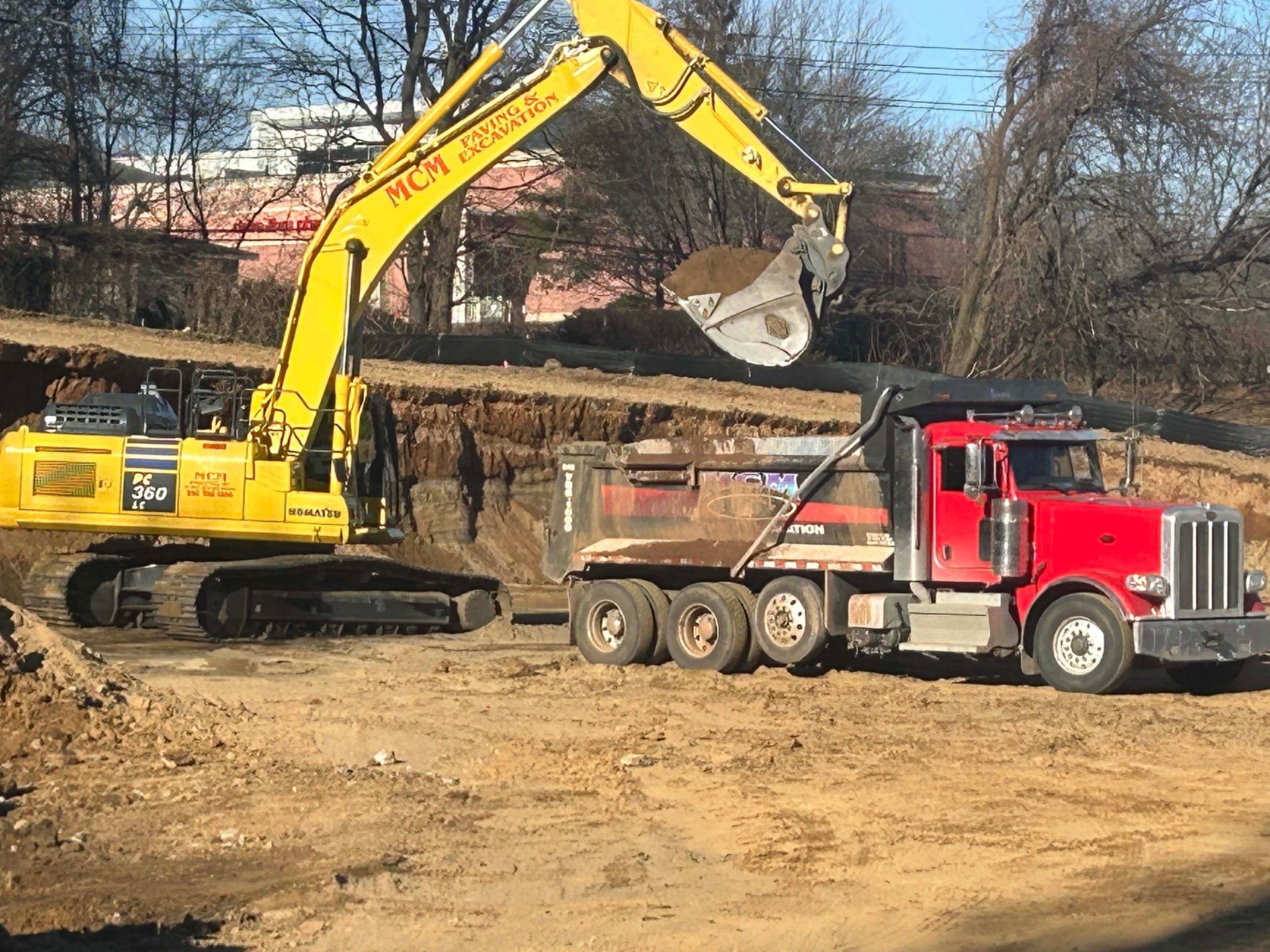A yellow excavator is loading dirt into a red dump truck.