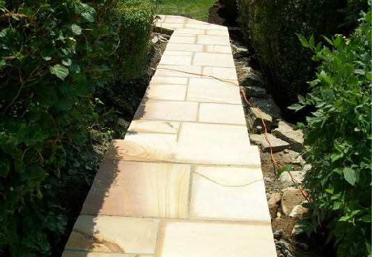 A walkway made of bricks is surrounded by trees and bushes.