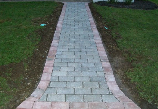 A brick walkway going through a lush green field.