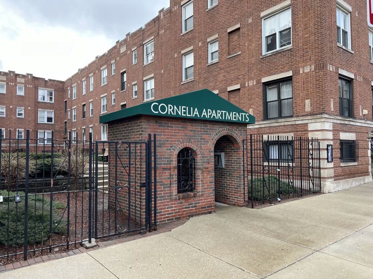A brick building with green awning, black metal gate and fence
