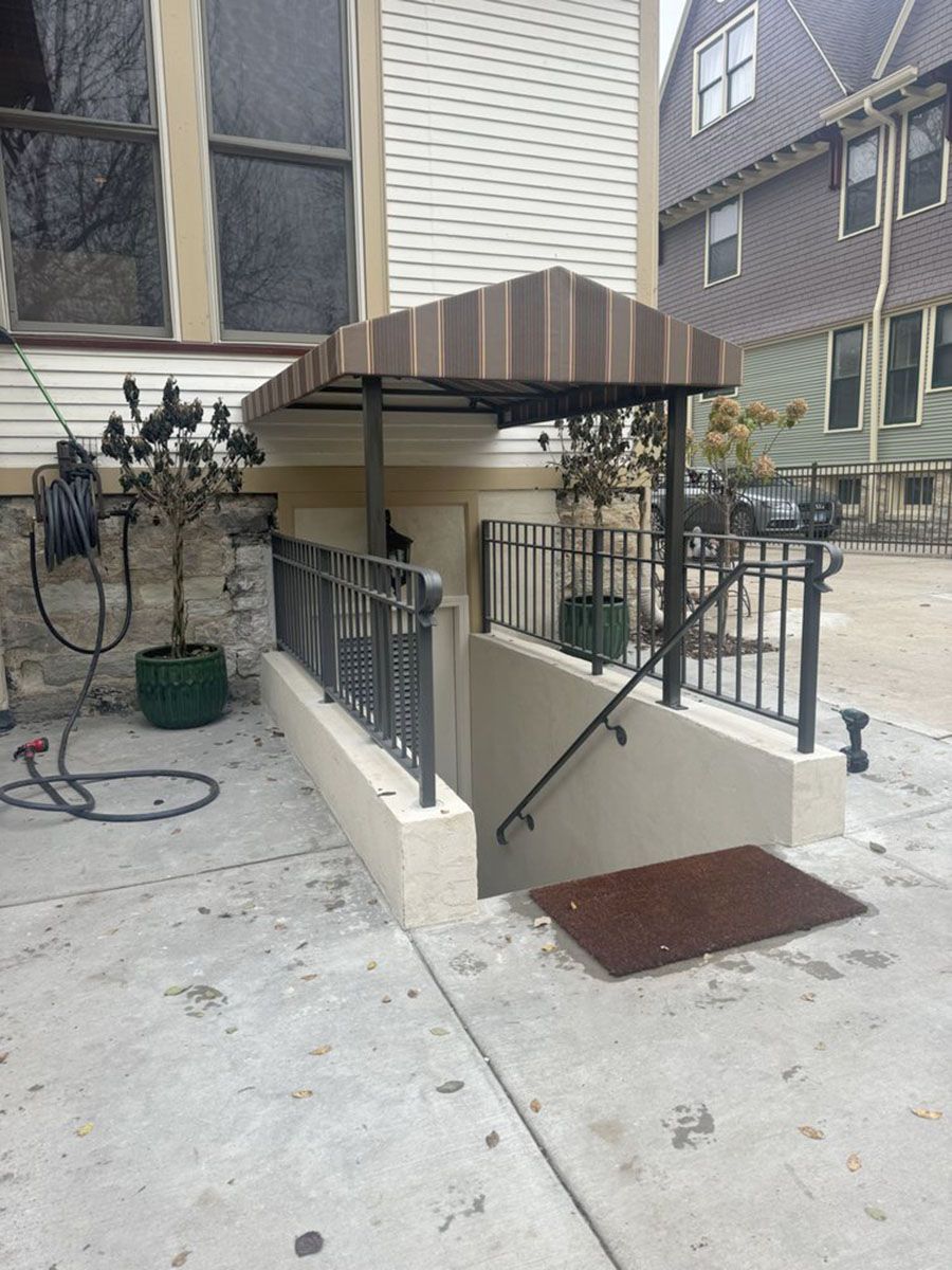 Exterior view of a building's basement entrance with stairs, metal railing, and an awning